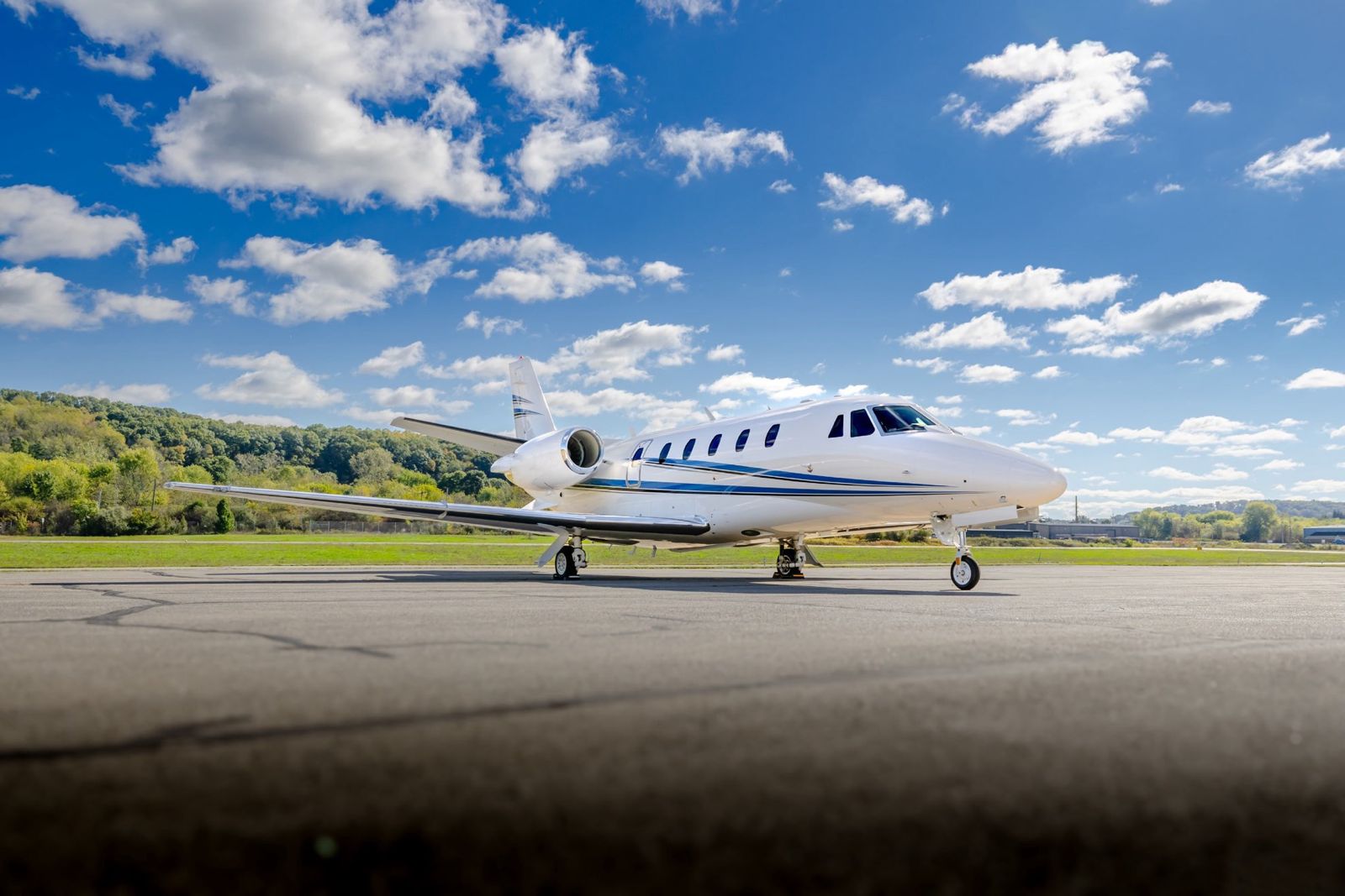 White midsize jet with blue stripes parked on an airport apron
