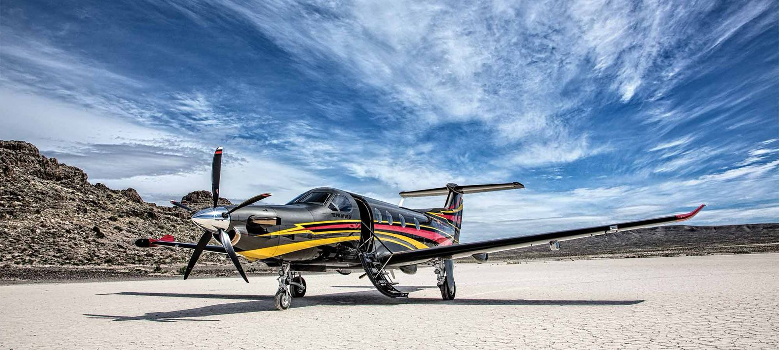 Single-engine turboprop parked with its boarding stairs open beside rocky terrain